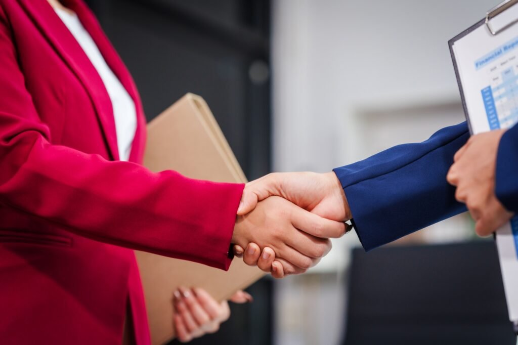 Two Asian businesswomen shake hands, collaborating on financial matters, discussing comments